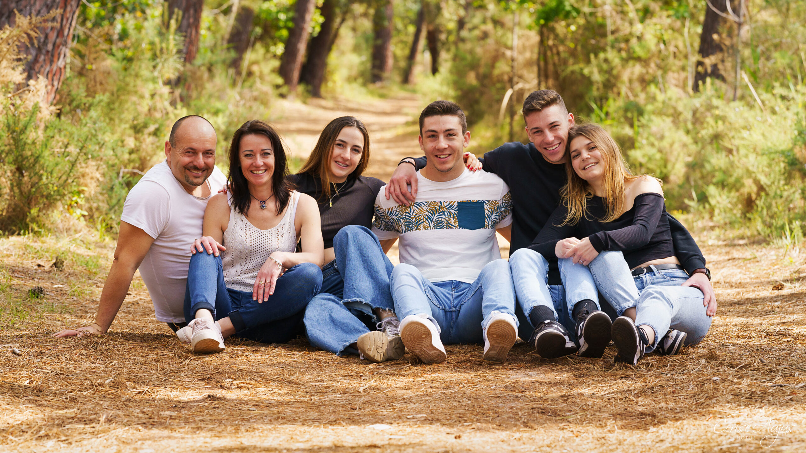 Famille complice : des parents et de leurs enfants assis en cercle dans la forêt de la Malloueyre à Mimizan, se tenant par les épaules et la taille lors d’une séance photo famille