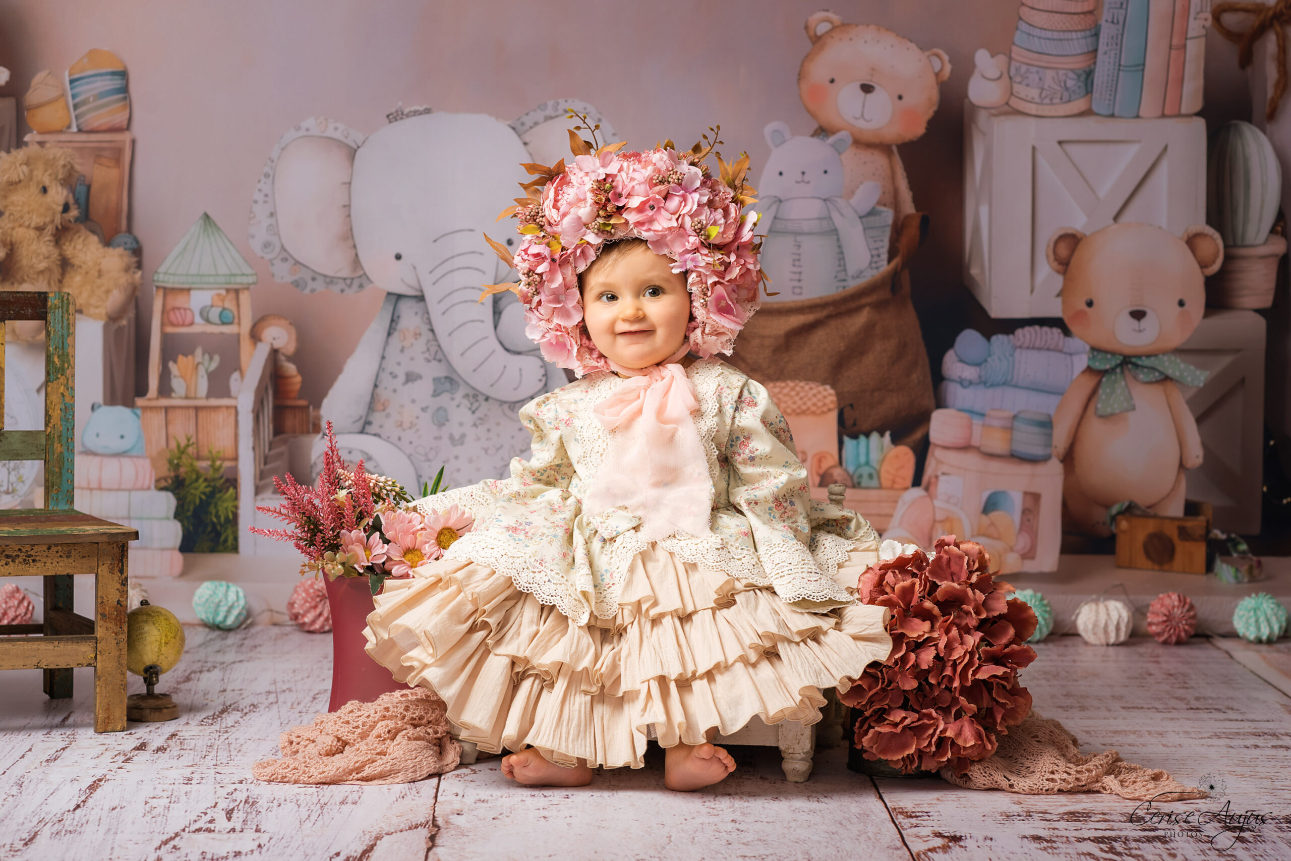 Petite fille en robe à froufrous dans décor chambre d’enfants assise sur chaise nounours livres jouets