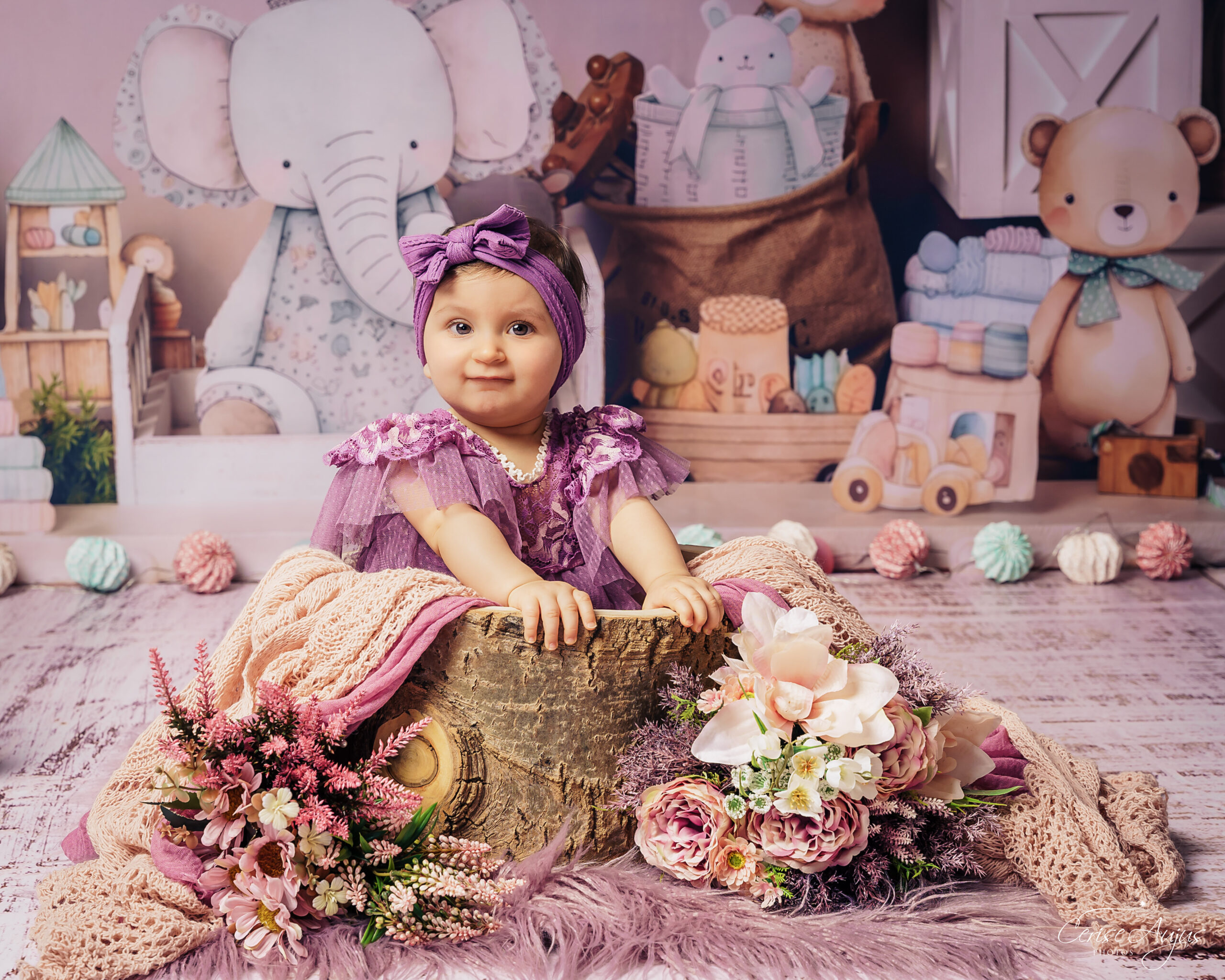 Petite fille en robe mauve dans décor chambre d’enfants assise dans un baquet en bois nounours livres jouets