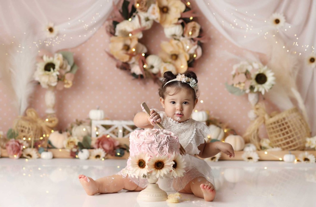 Petite fille souriante dégustant smash cake dans décor bohème automnal rose et crème