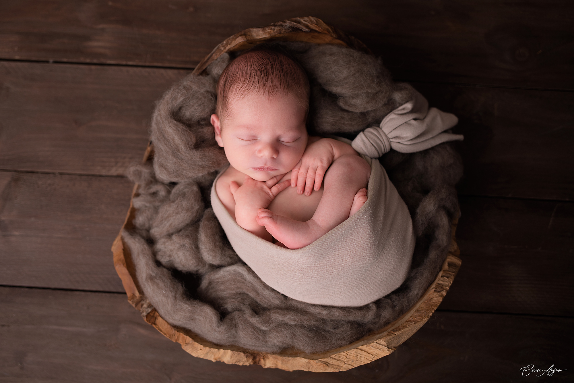 Bébé endormi sur le dos en position cocon dans un contenant lors d’une séance photo naissance à Mimizan