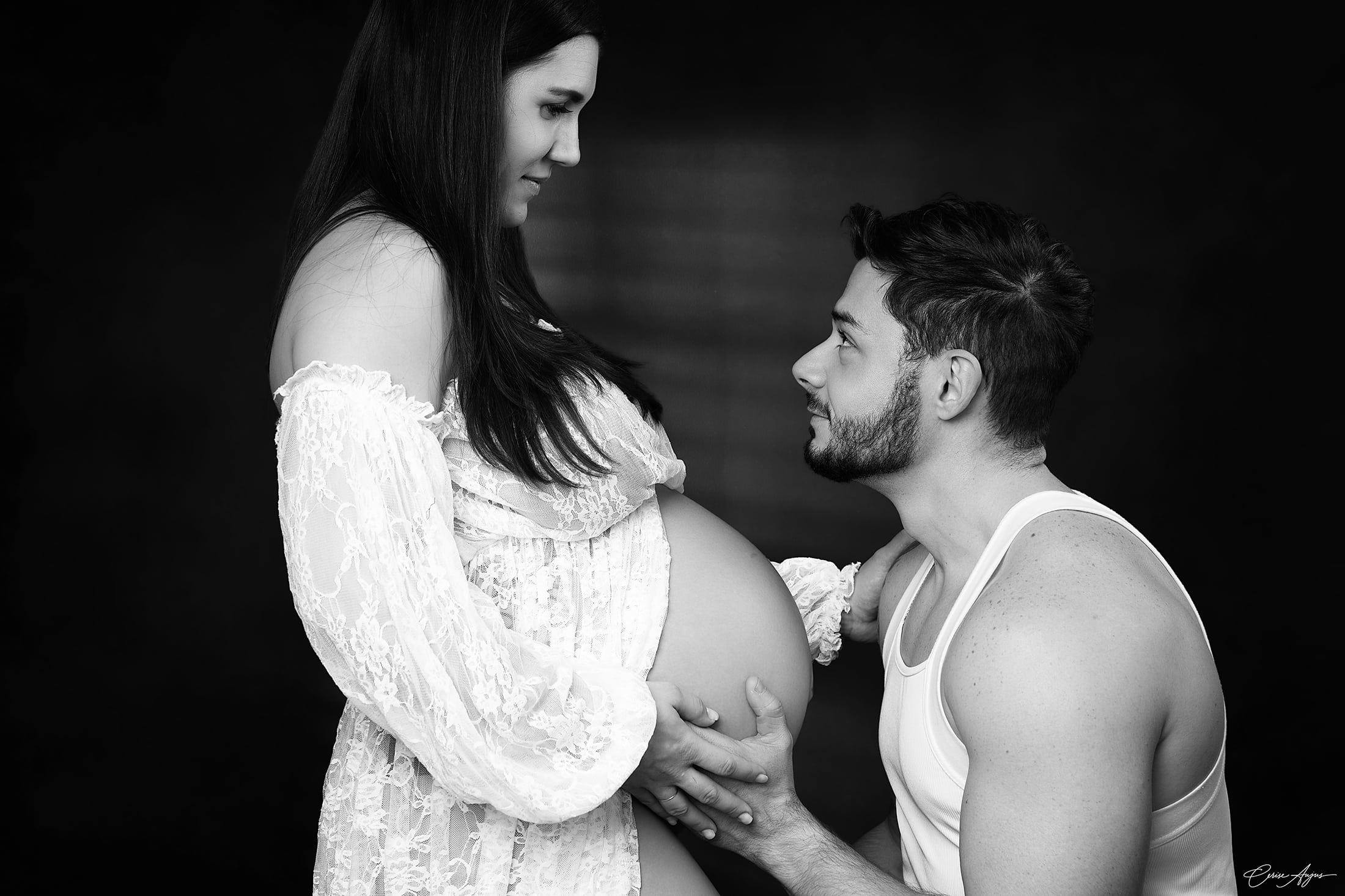 Séance photo grossesse en couple dans les Landes en noir et blanc : conjoint agenouillé tenant le ventre rond de sa compagne, regards complices — studio Cerise Aujus Photos