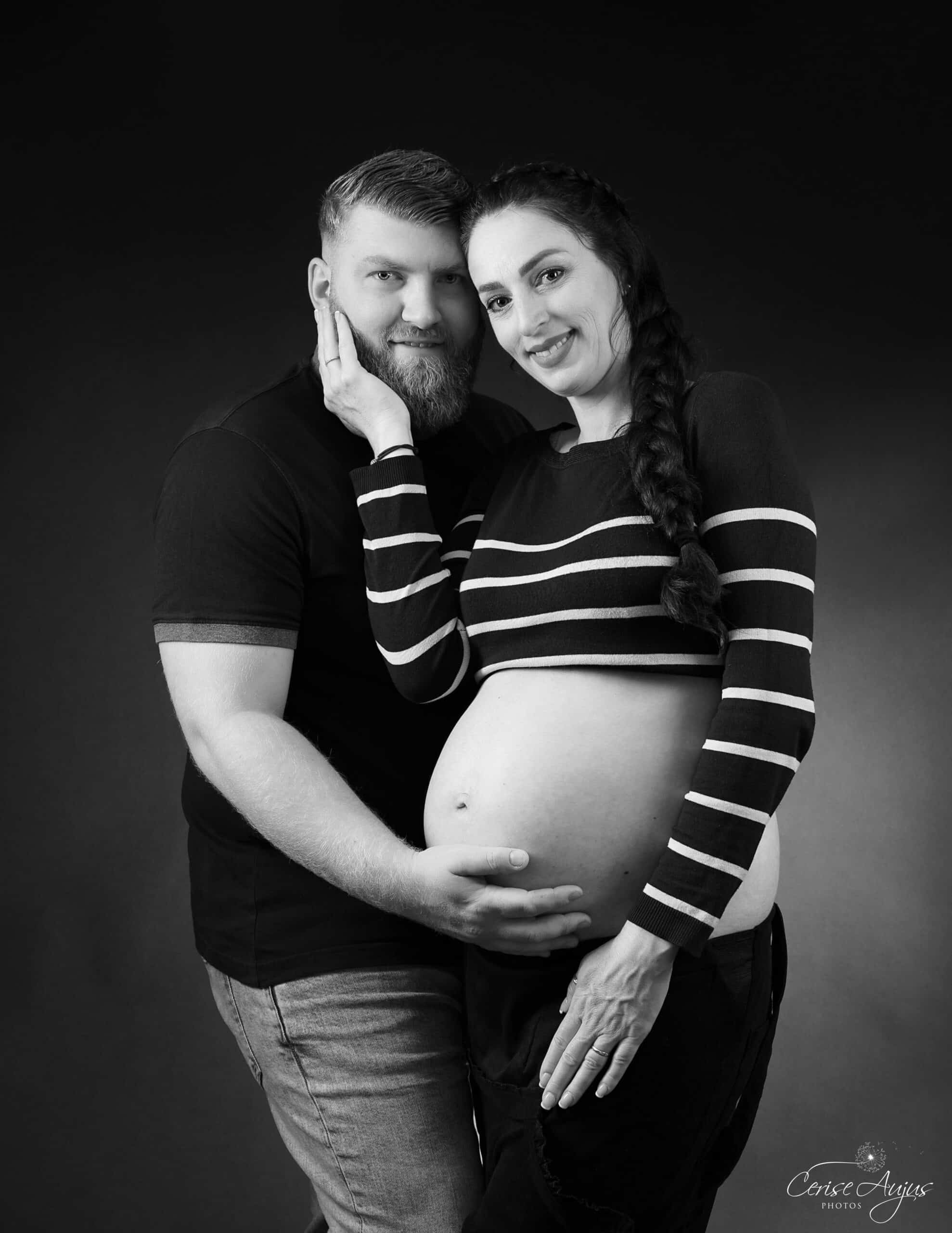 Séance photo grossesse en couple dans les Landes en noir et blanc : femme enceinte appuyée contre son conjoint, main sur sa joue, sourires face à l'objectif — Cerise Aujus Photos Pontenx