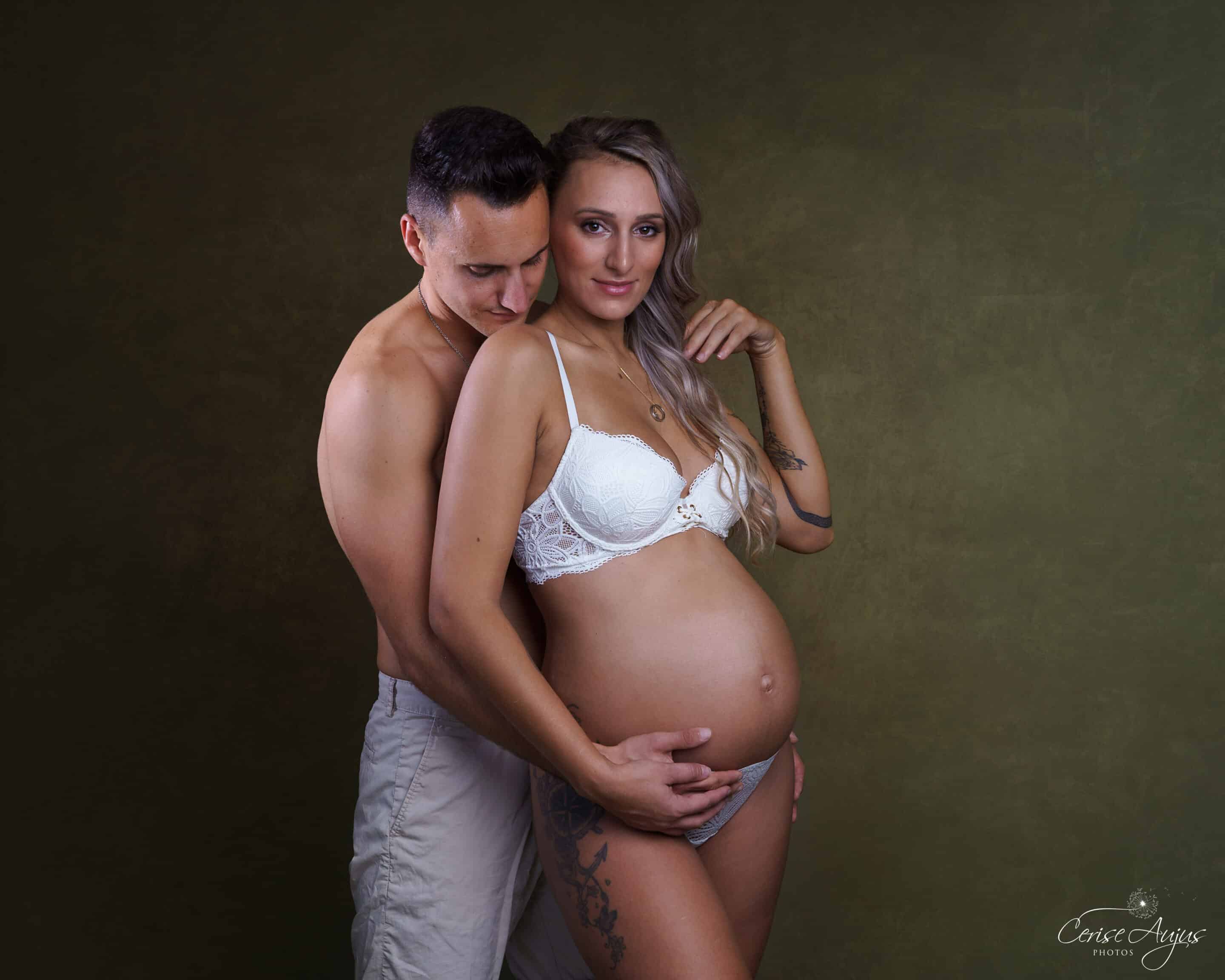 Couple enceinte en studio, future maman en lingerie blanche enlacée par son compagnon, séance photo grossesse près de Biscarrosse dans les Landes