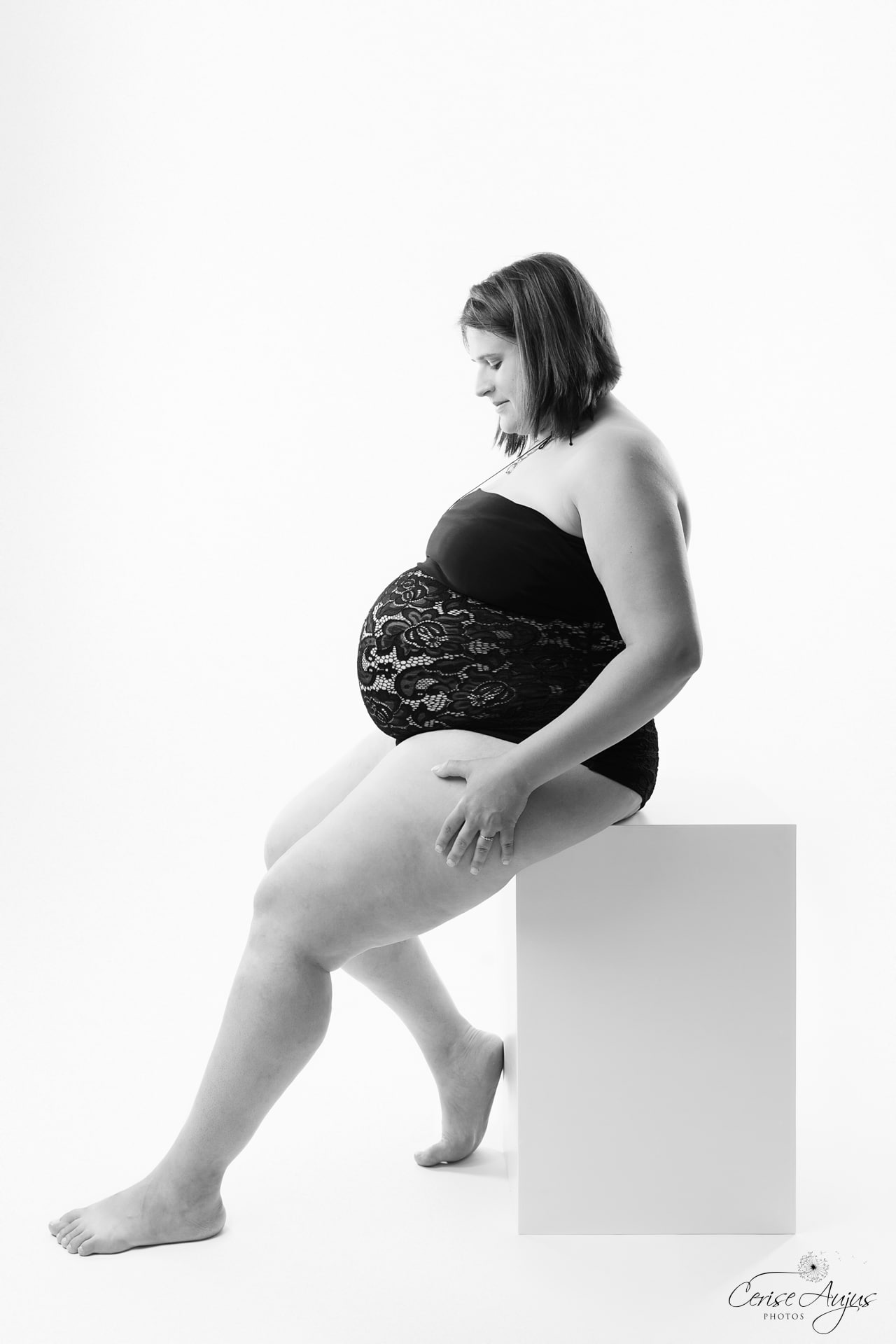 Femme enceinte en body dentelle noire assise sur un cube blanc, séance photo grossesse en studio près de Biscarrosse dans les Landes