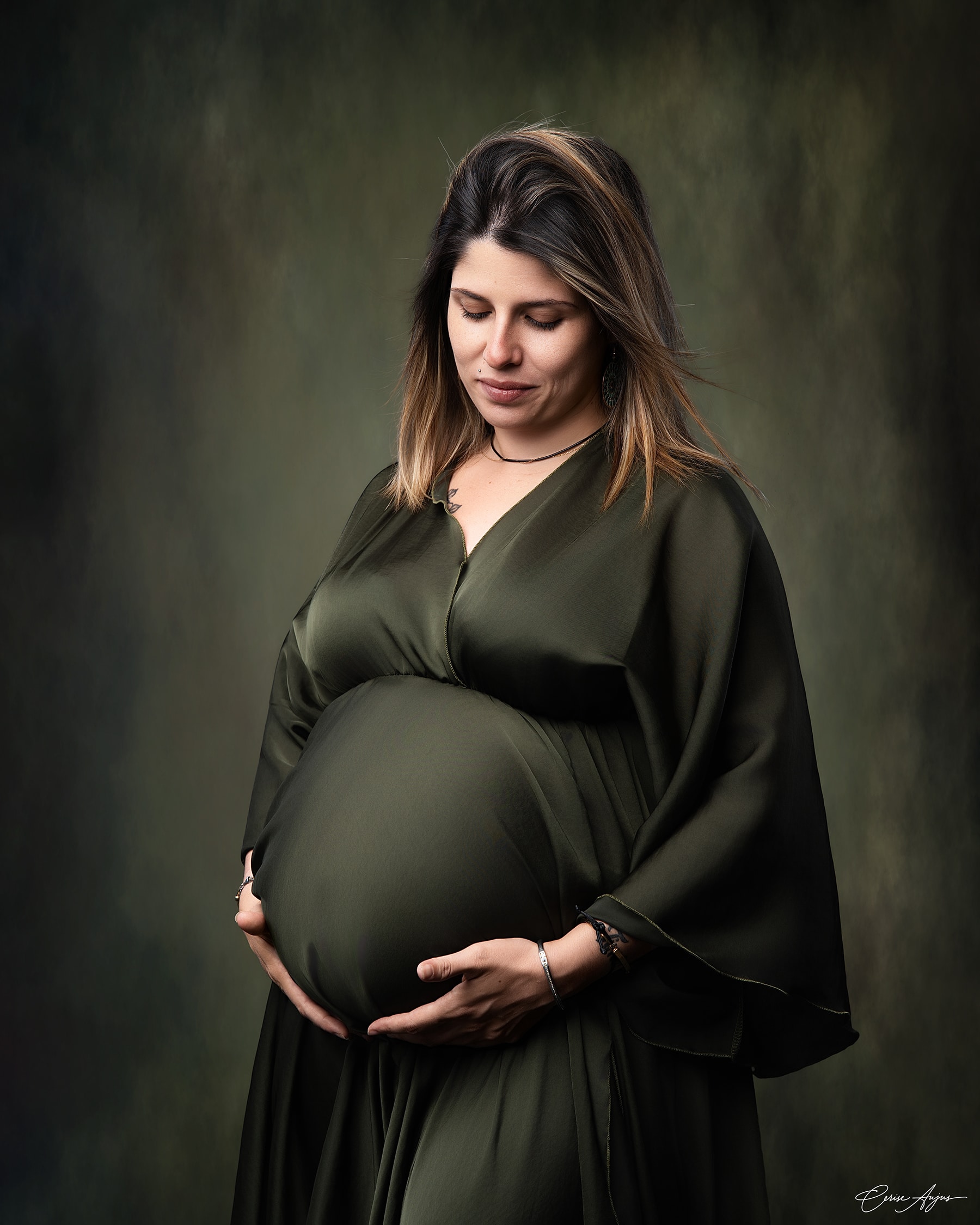 Femme enceinte en robe verte tenant son ventre, séance photo grossesse en studio dans les Landes
