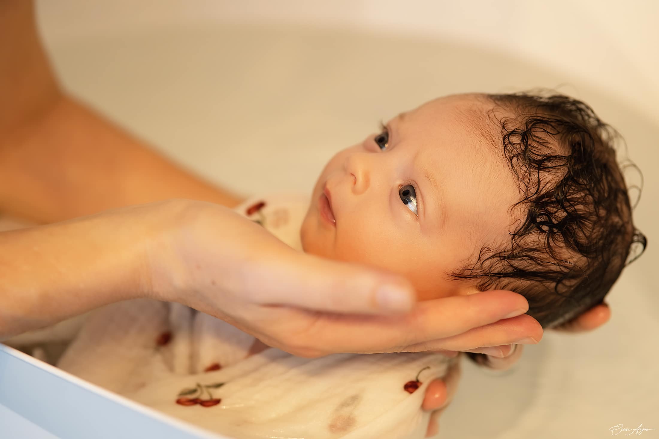 Nouveau-né porté dans l'eau par la praticienne, regard ouvert et éveillé, pendant un bain thérapeutique bébé