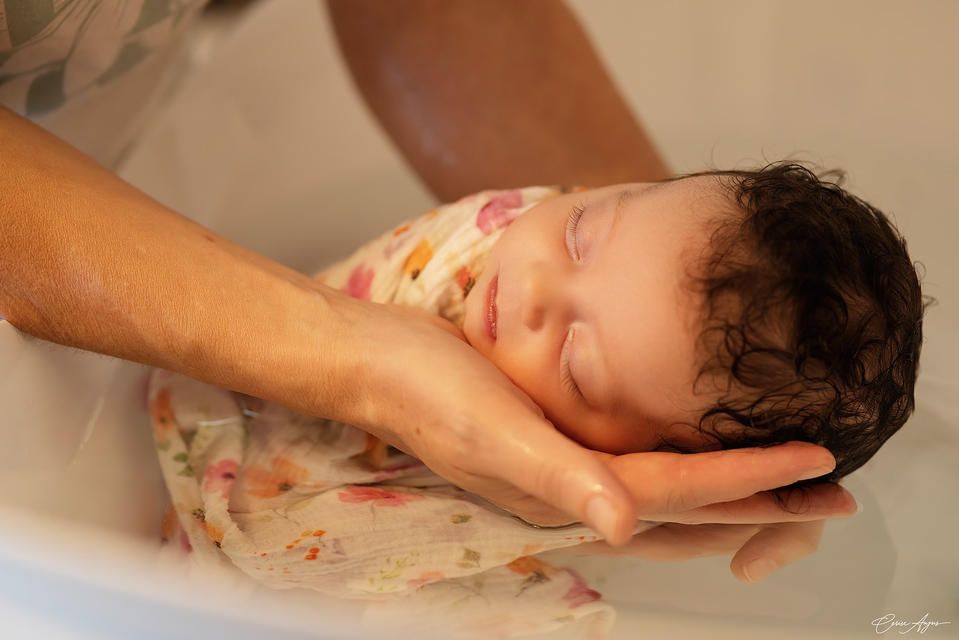 Nouveau-né endormi et emmailloté dans les bras de la praticienne pendant un bain thérapeutique bébé