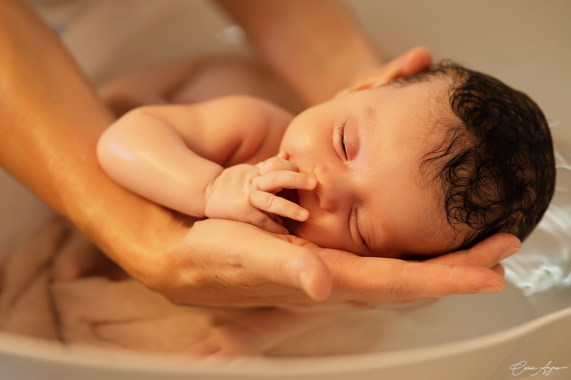 Nouveau-né lové dans les mains de la praticienne pendant un bain thérapeutique bébé - photographe Landes