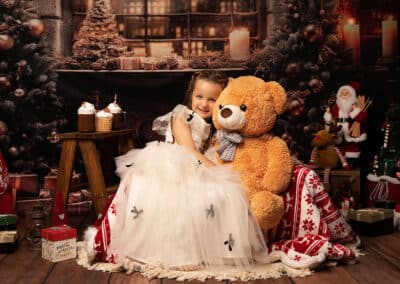 Photographe Noël Landes, décor La Veillée de Noël, enfant en robe blanche câlinant un ours en peluche en studio à Pontenx-les-Forges